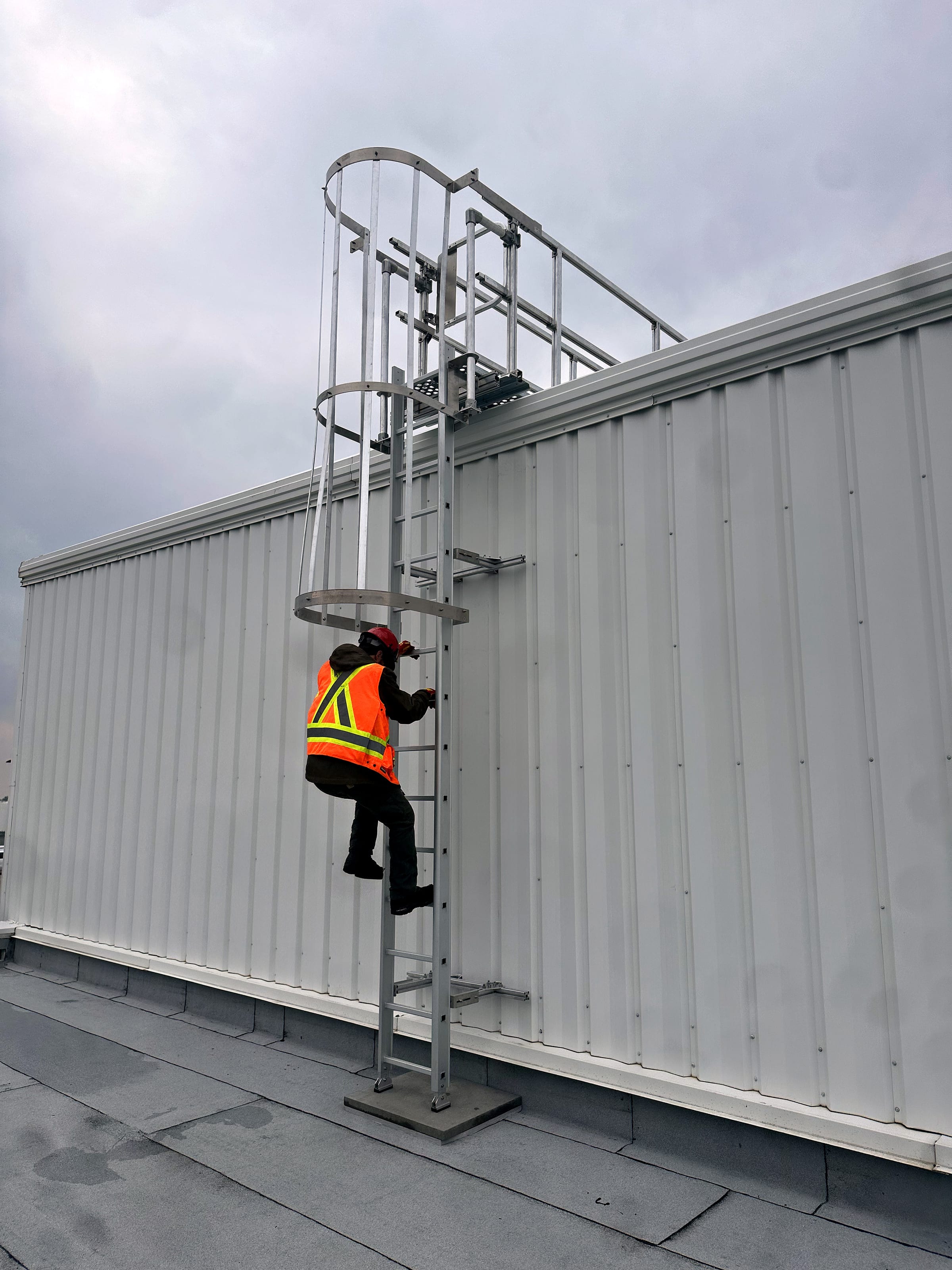 Worker climbing a caged ladder to a rooftop guardrail platform.