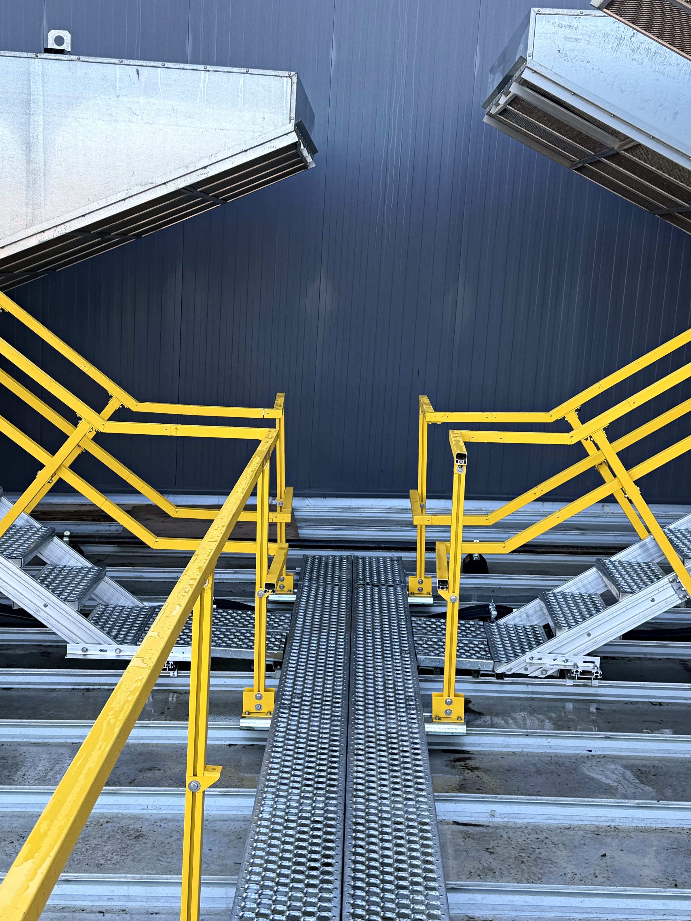 Safety-yellow guardrail and stairs leading to rooftop units, upward angle.